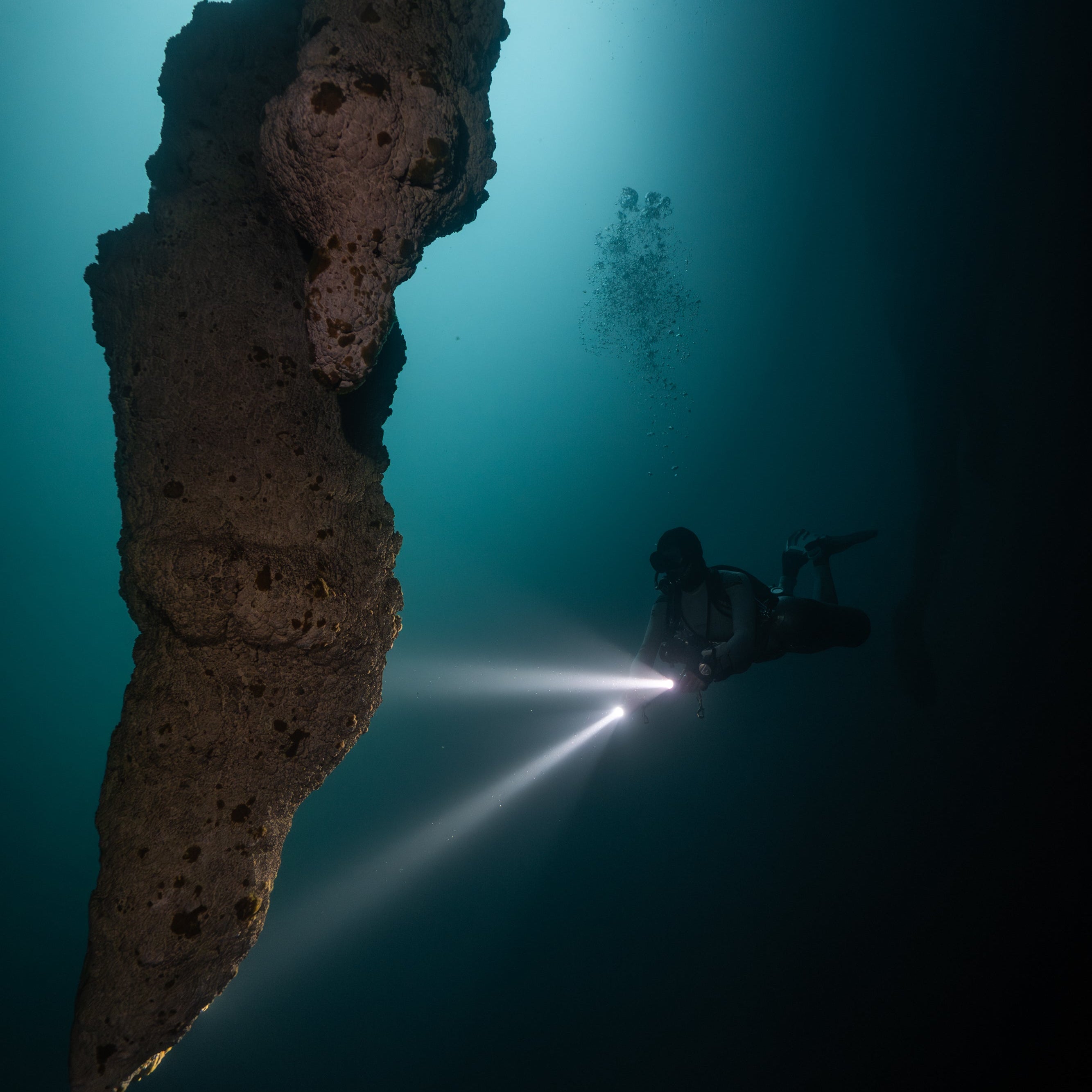 Diver exploring a dark underwater cave with a flashlight.